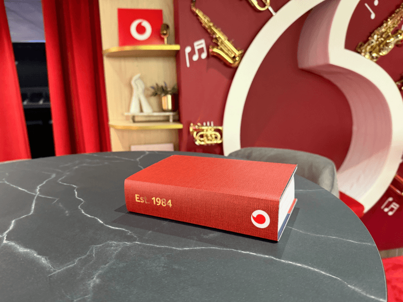 Red Vodafone Est 1984 book on a marble table in the lounge, with gold instruments on the wall behind