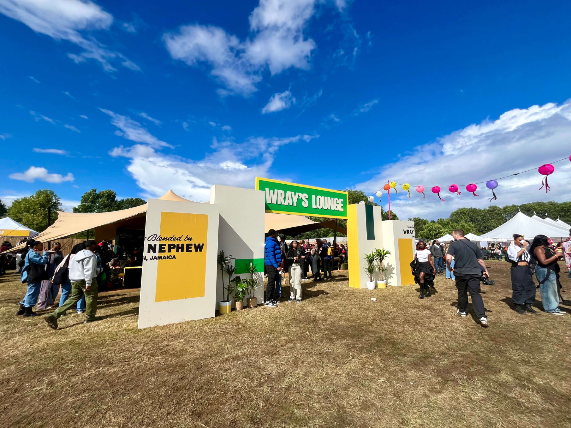 Wray's Lounge festival entrance with branded pillars, flags and guests gathered outside