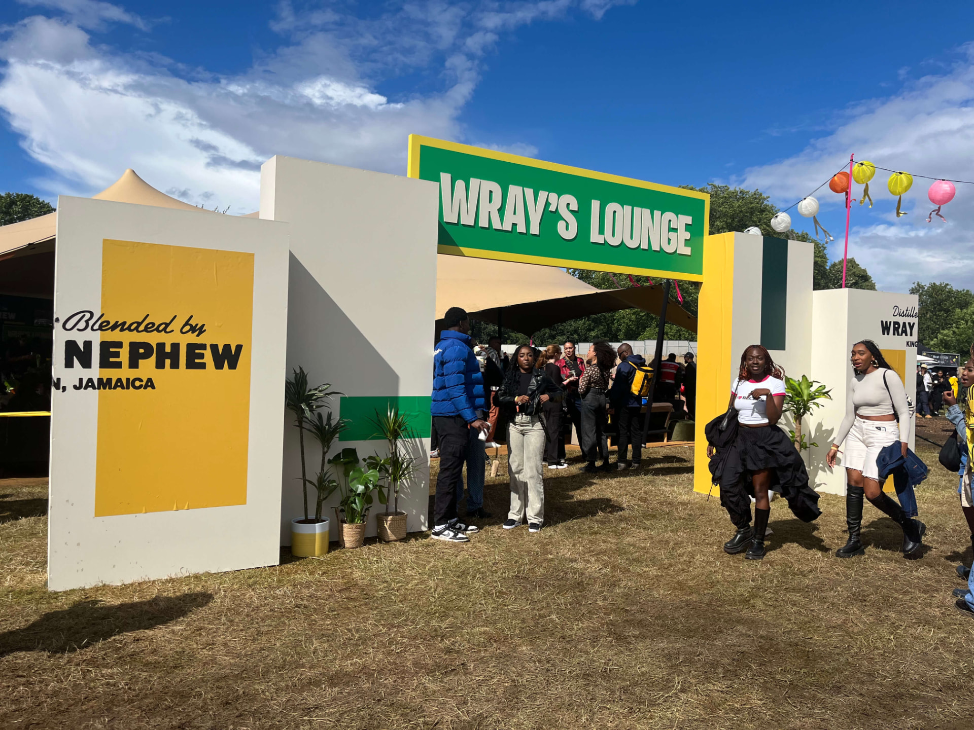 Wray's Lounge entrance pillars in white, yellow and green beneath the Wray's Lounge sign, leading to the tent