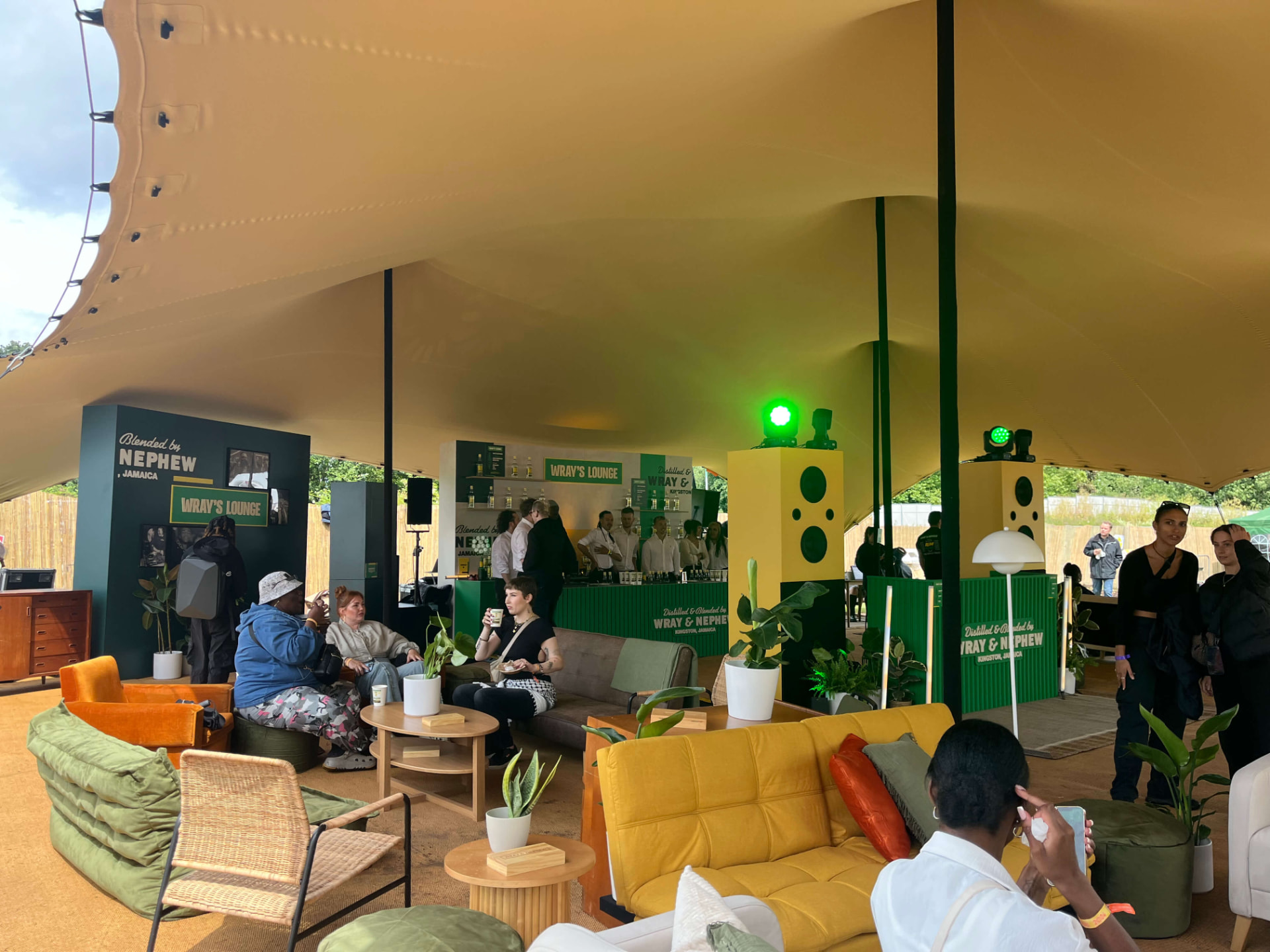 Inside the Wray's Lounge tent with colourful sofas, potted plants and yellow speaker towers