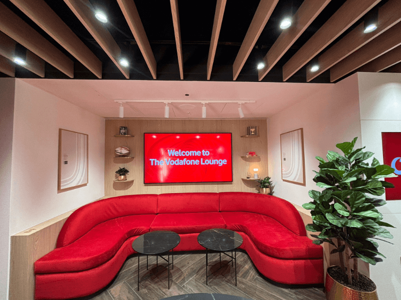 Curved red sofa in The Vodafone Lounge beneath a screen reading Welcome to The Vodafone Lounge