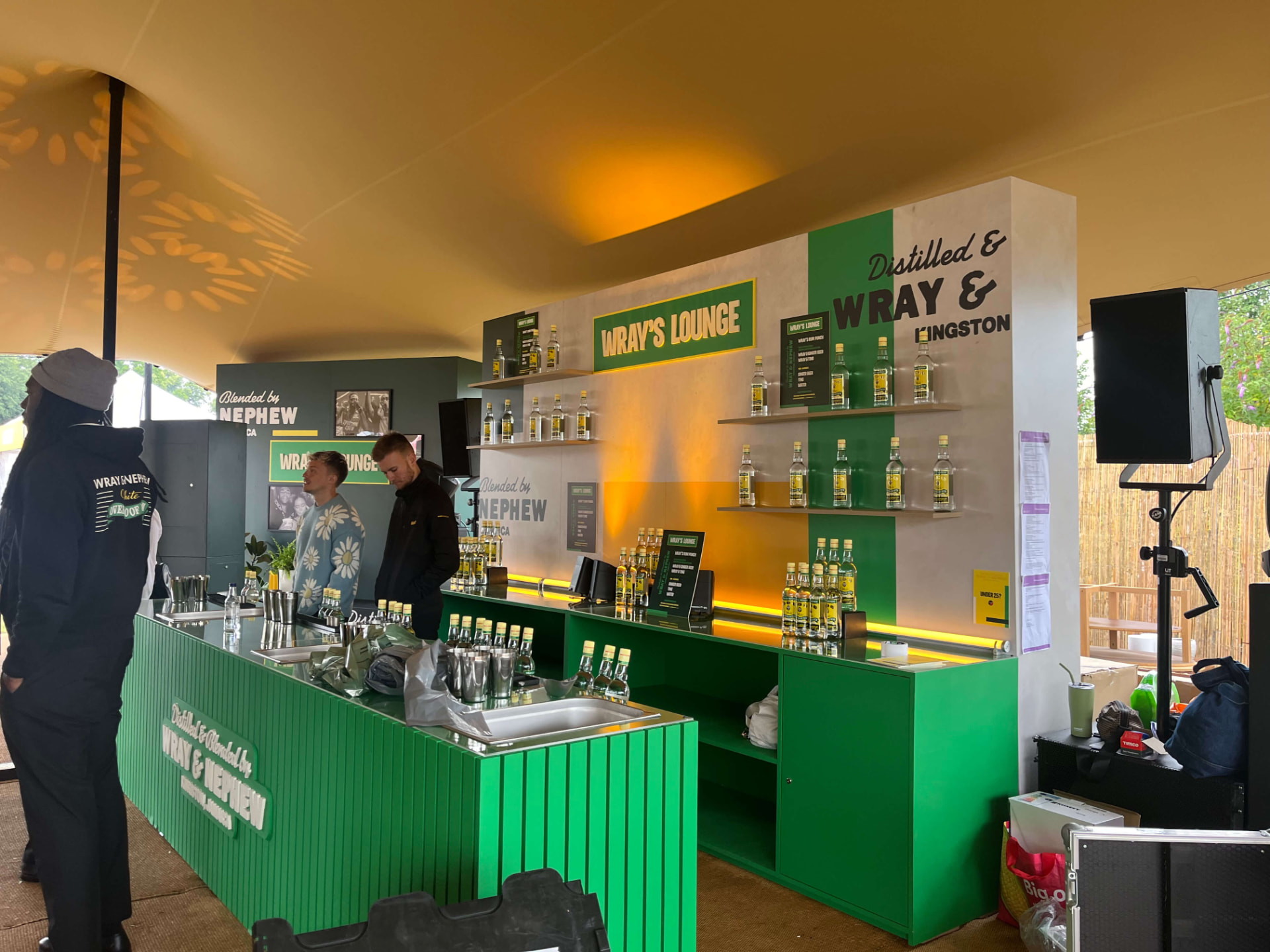 Green slatted Wray's Lounge bar under the tent, stocked with Wray & Nephew bottles and attended by staff