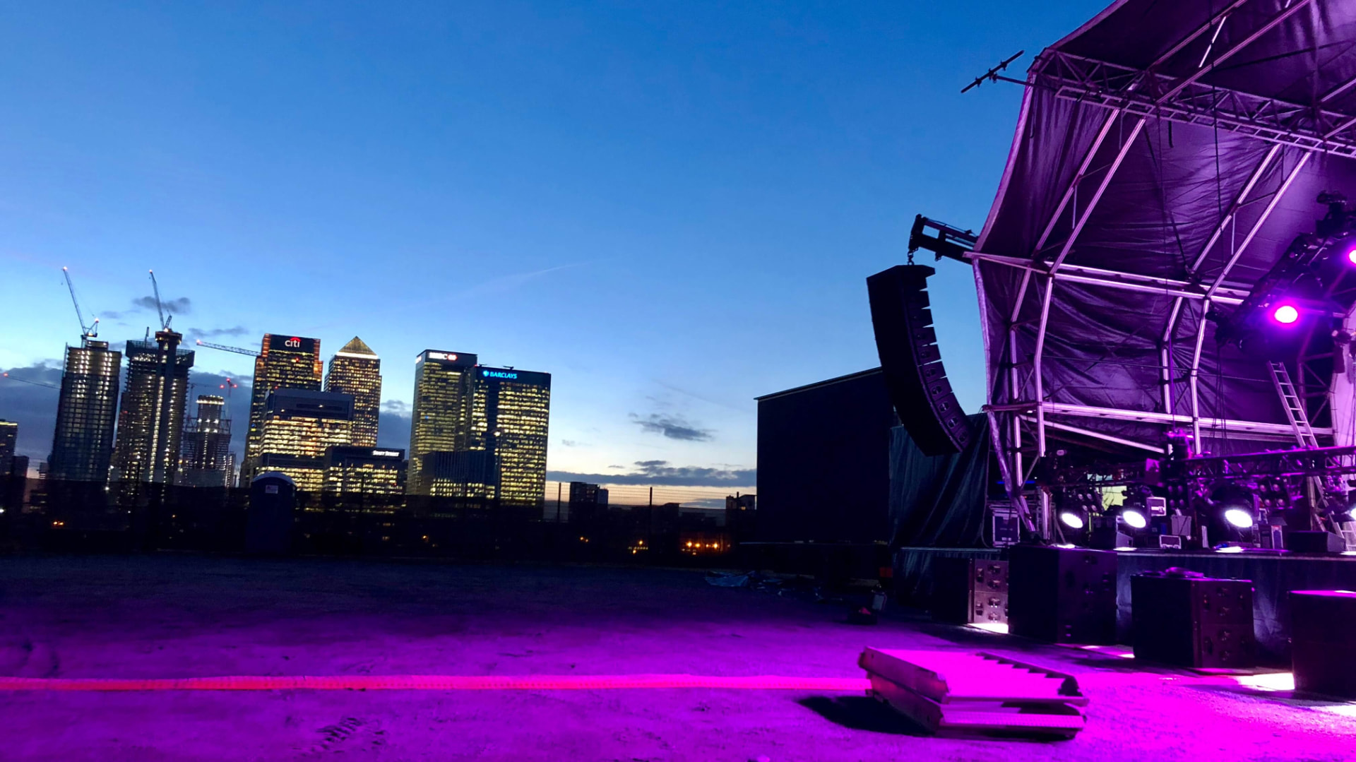 Outdoor event stage overlooking a city skyline at dusk, illuminated with purple production lighting